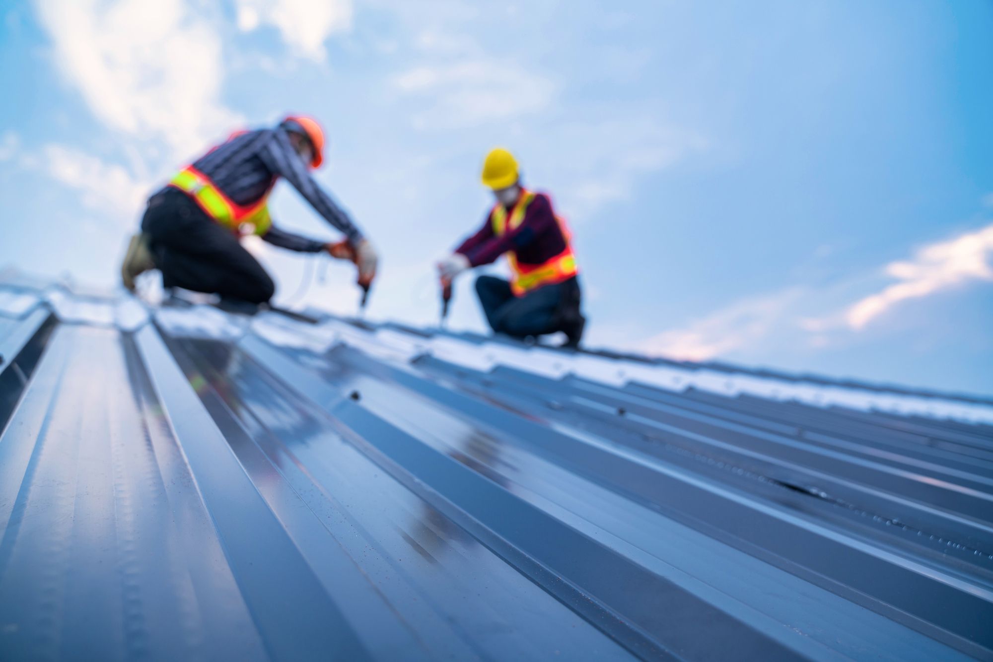 Zwei Arbeiter bei der Montage von Metalldächern, wobei der Schwerpunkt auf der reflektierenden Oberfläche liegt.